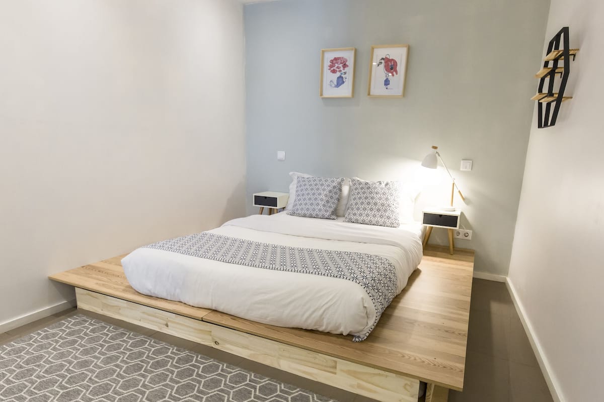 A bedroom with a bed, bedside tables, a lamp, and a wall-mounted shelf.