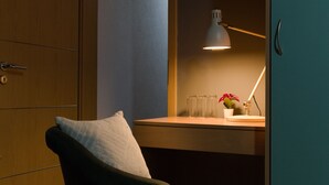 A room with a wooden wardrobe, a desk with a lamp, a chair, and a small potted plant. - Hotel Moment (Velika Plana)