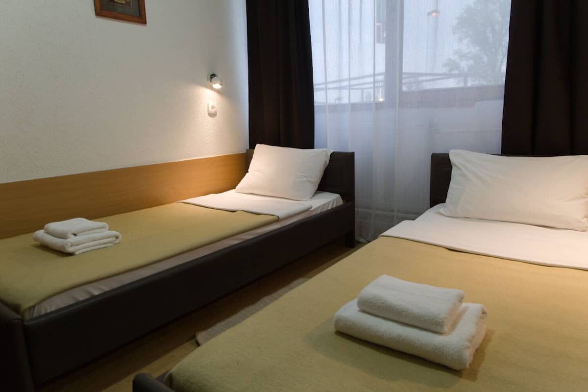A hotel room with two single beds, each with a pillow and a folded towel.