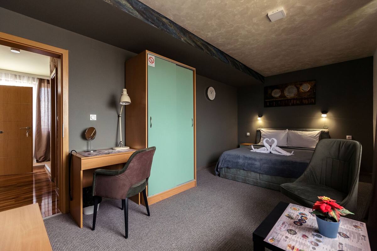 A compact hotel room with a desk, chair, bed, and a small table with a plant.