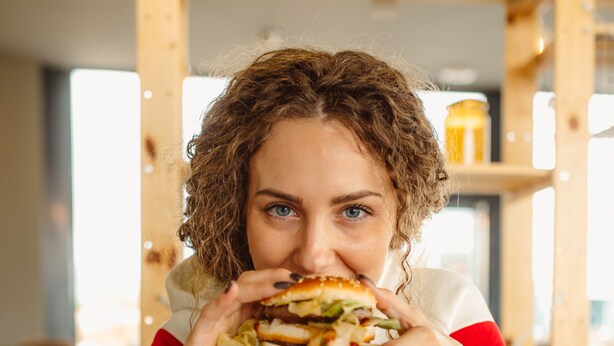 A person sitting at a table with a burger and fries, a Coca-Cola cup, and a menu. - Hotel Moment (Velika Plana)