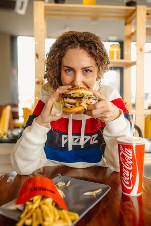 A person sitting at a table with a burger and fries, a Coca-Cola cup, and a menu. - Hotel Moment (Velika Plana)