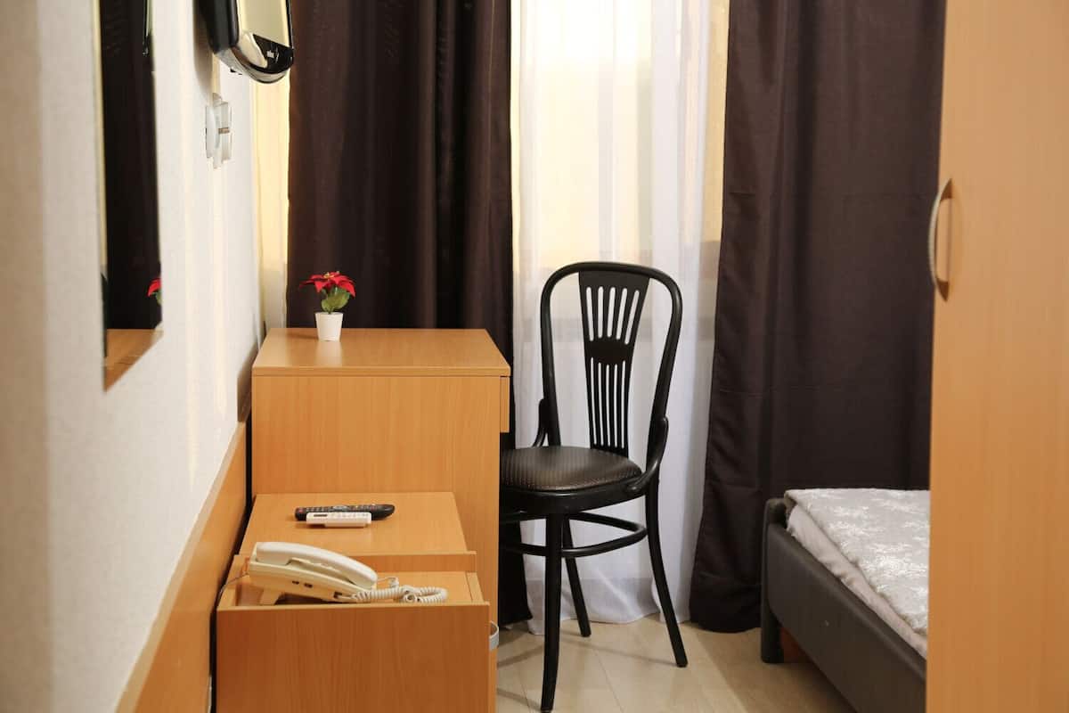 A small hotel room with a wooden desk, a black chair, a bed, and a small potted plant.