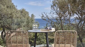 Et flettet bord med stole, et glas vand og en bog på en balkon med udsigt over vandet.