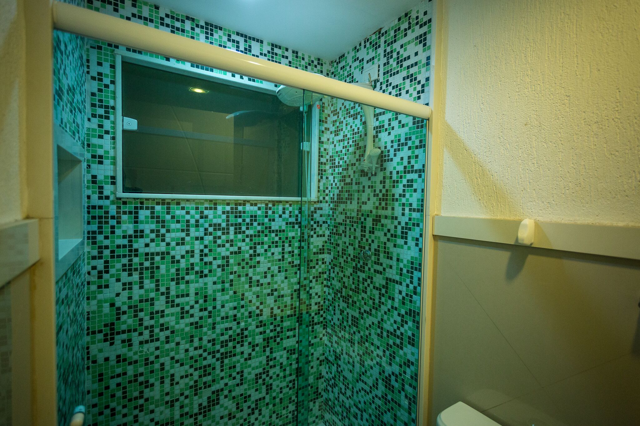 A bathroom with mosaic tile walls, a window, and a toilet.