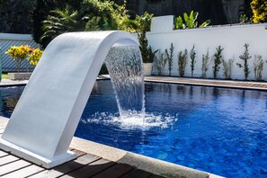 Ein Swimmingpool mit Wasserfall, umgeben von einer weißen Mauer und Kübelpflanzen.