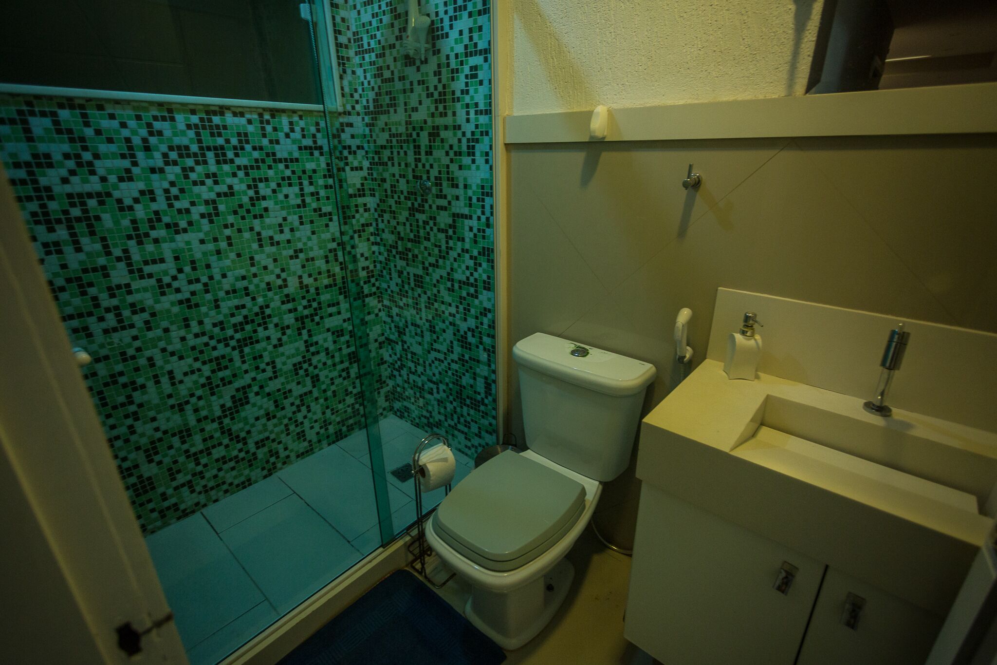 A bathroom with a mosaic-tiled shower wall, a toilet, and a sink with a mirror.