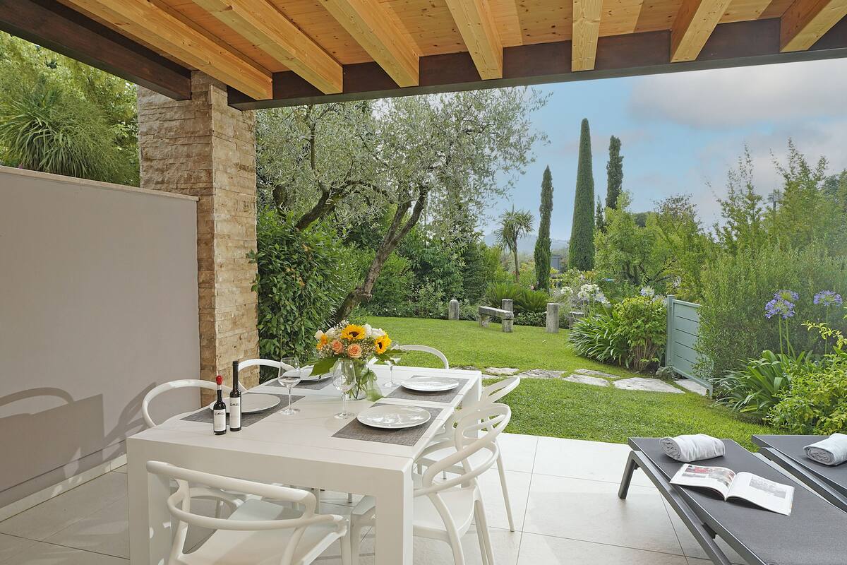 An outdoor dining area with a table set for two, a bottle of wine, and a vase with flowers.