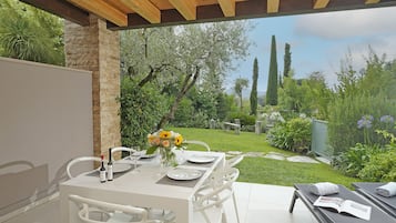 An outdoor dining area with a table set for two, a bottle of wine, and a vase with flowers.