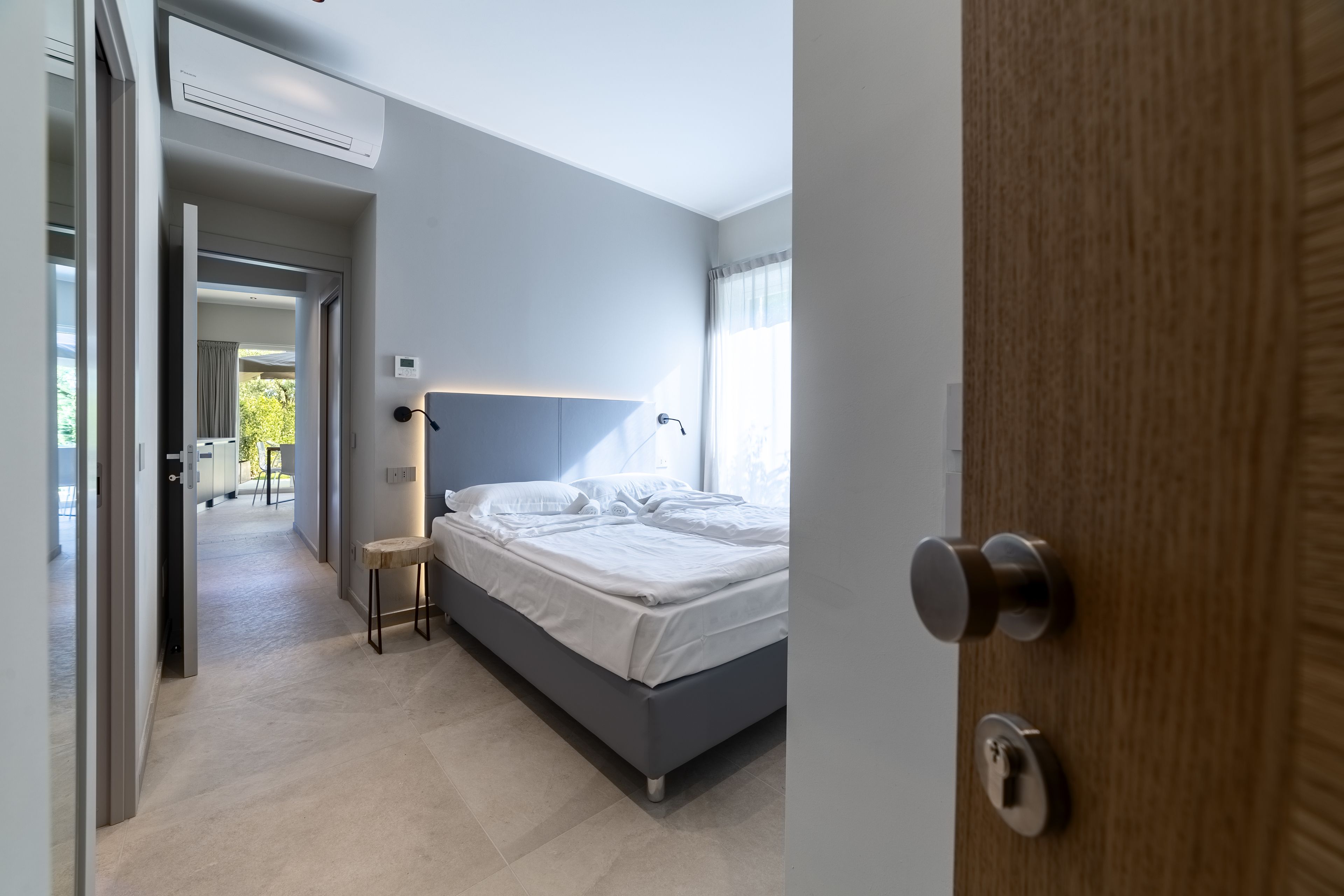 A modern bedroom with a bed, bedside table, and a view of the outdoors.