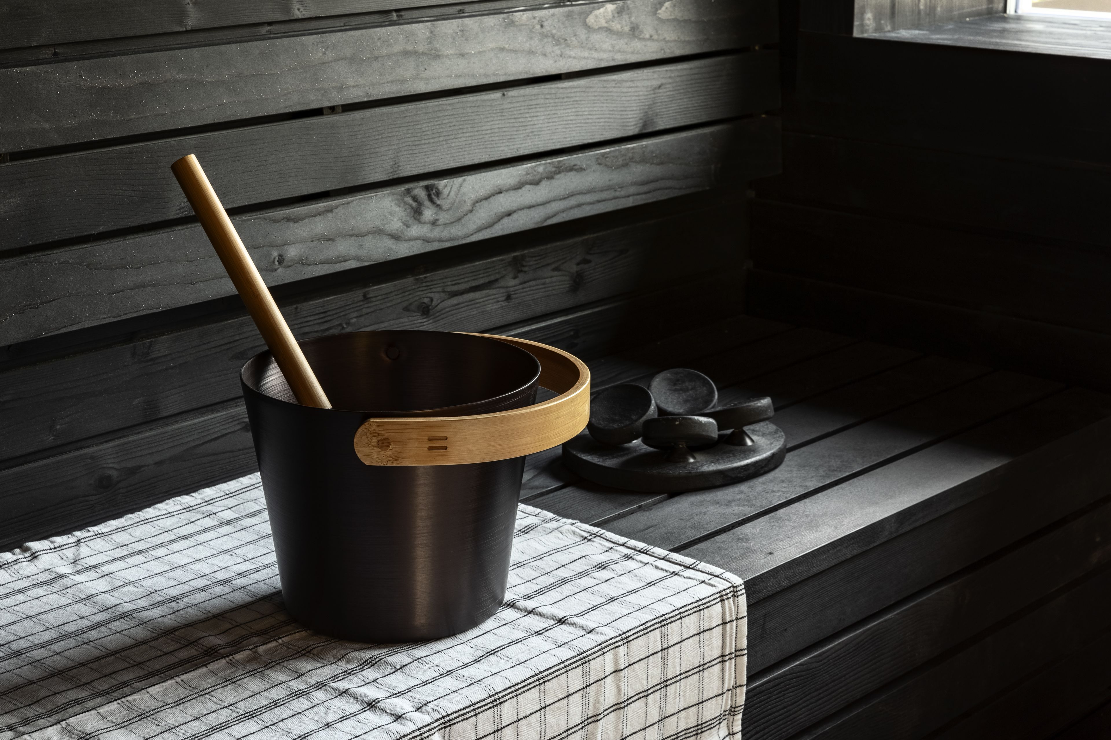A kitchen with a black pot on a wire rack, a wooden spoon inside, and a wooden cutting board on a black tray.