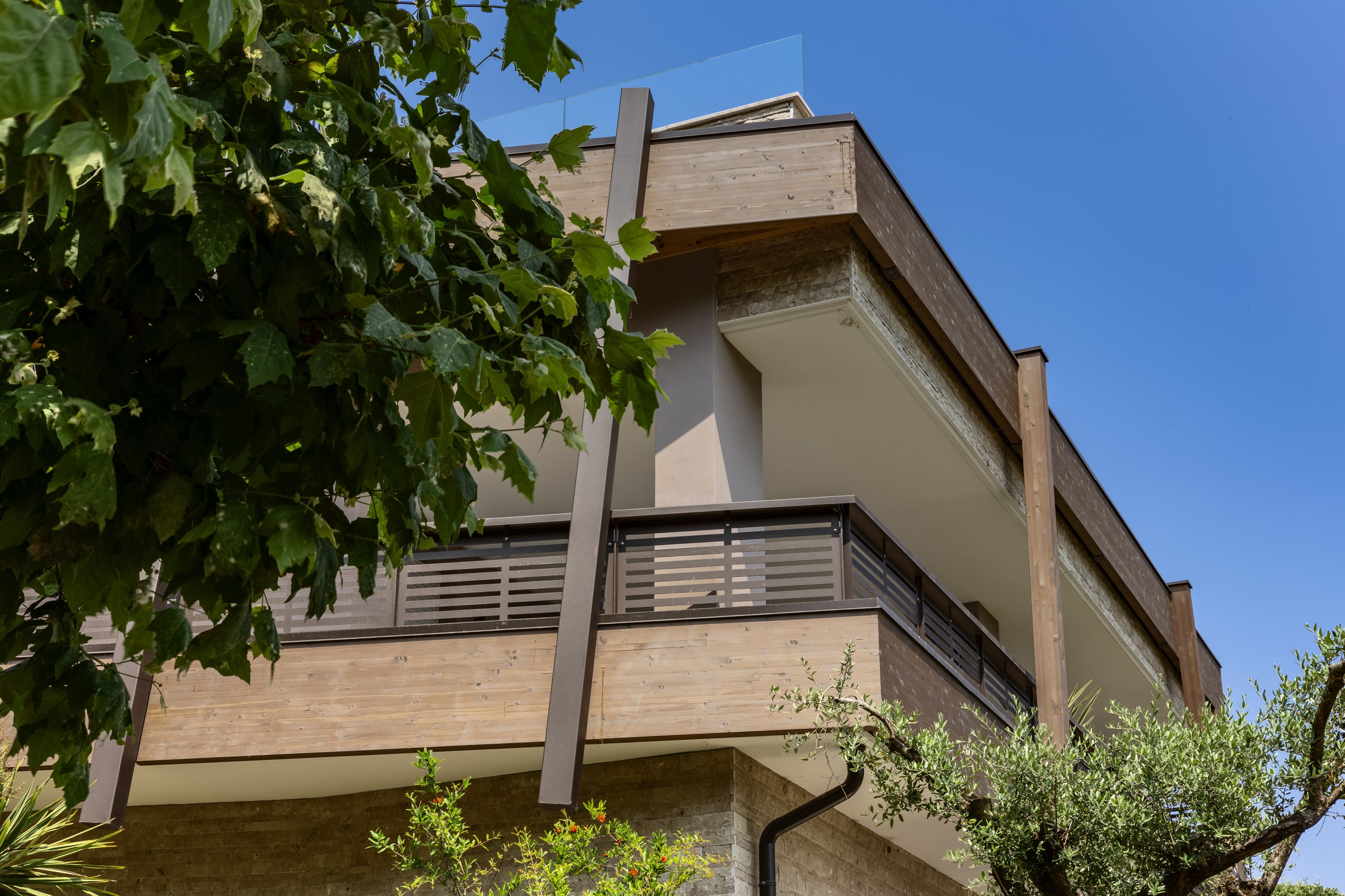 A multi-story building with a modern architectural design, featuring a balcony with metal railings and a wooden facade.