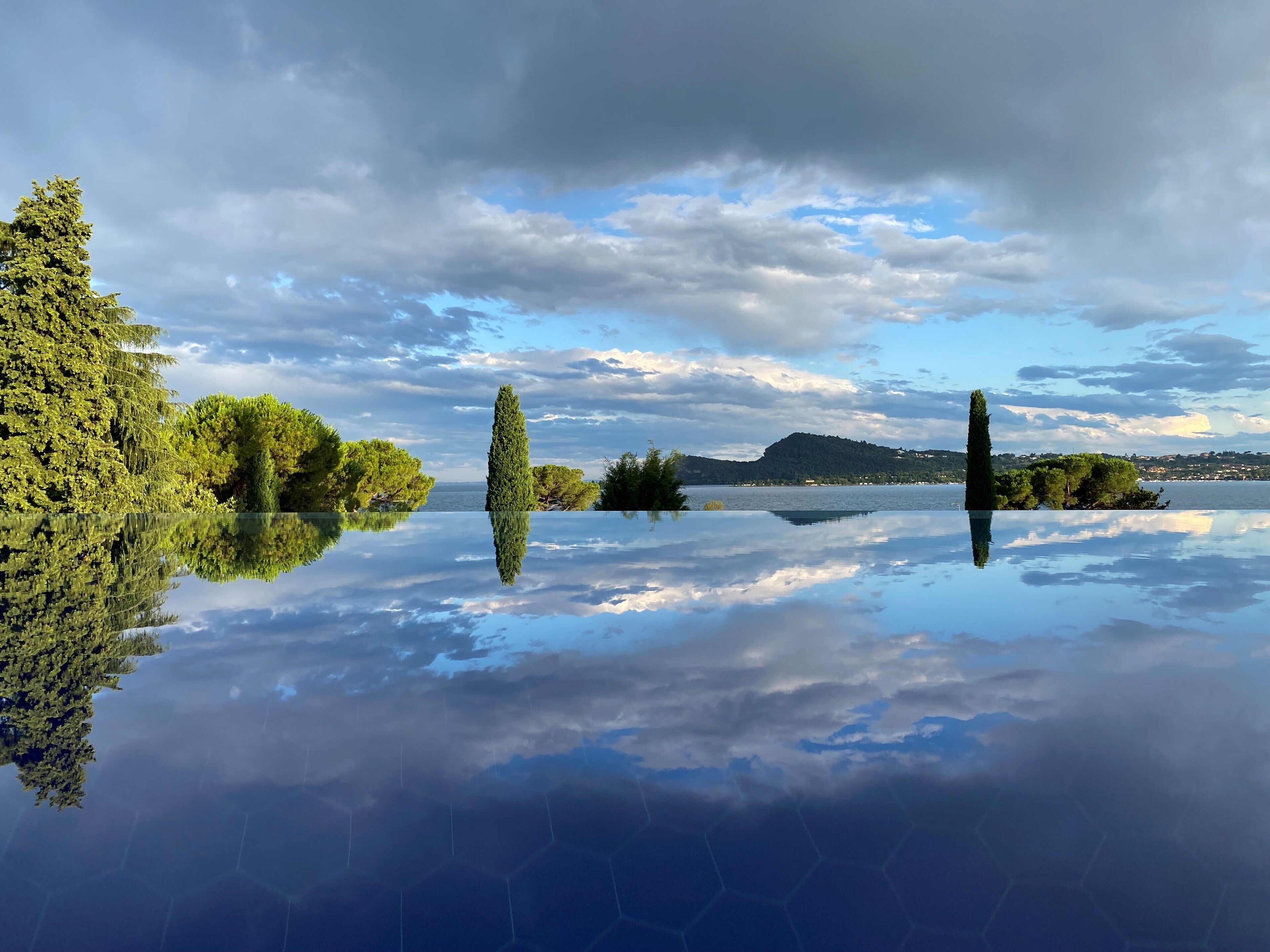 A calm lake with clear reflections of trees and a distant mountain range.