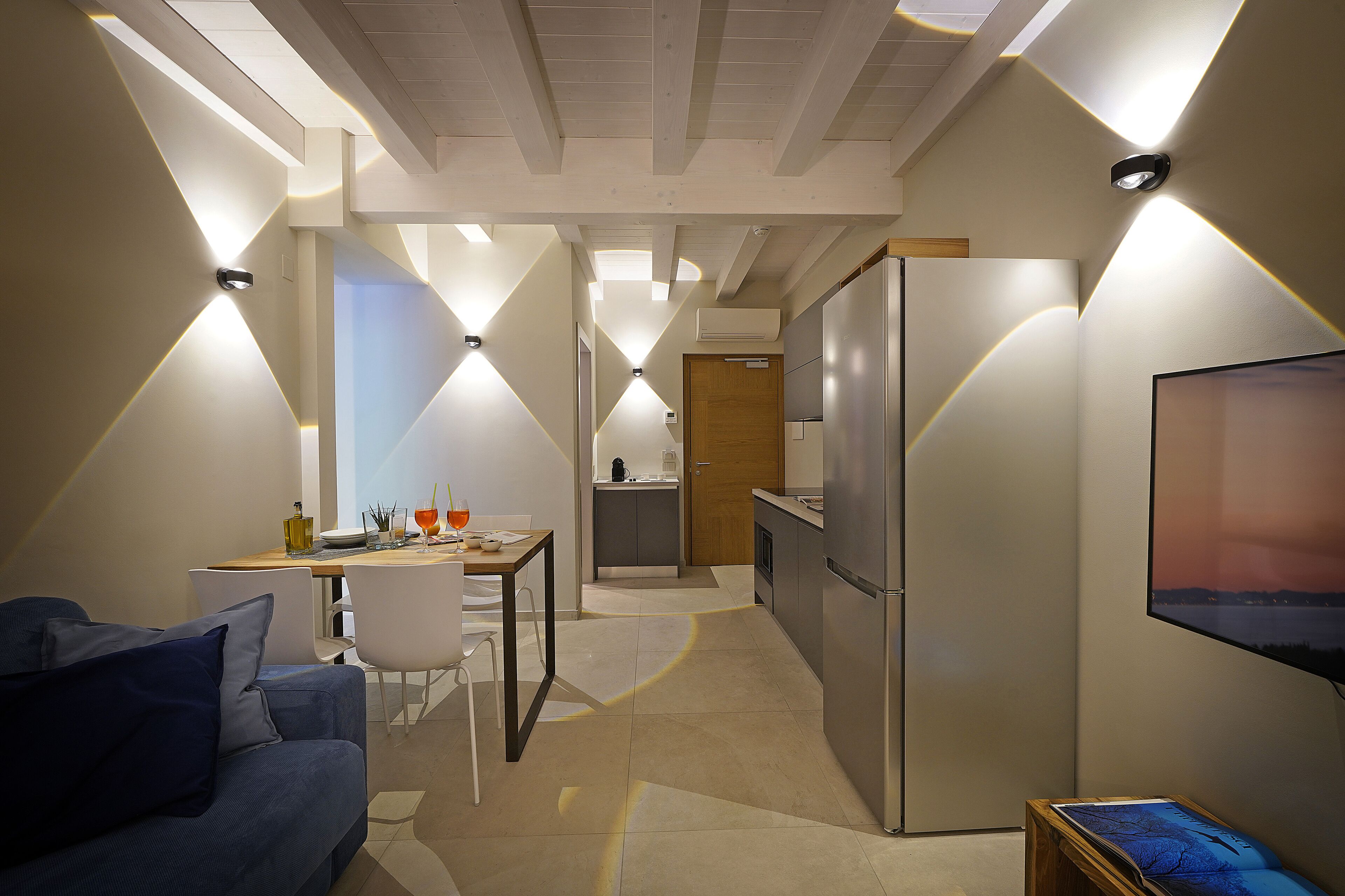 A modern kitchen with a refrigerator, a dining area with a table and chairs, and a living area with a sofa.