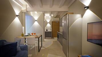 A modern kitchen with a refrigerator, a dining area with a table and chairs, and a living area with a sofa.
