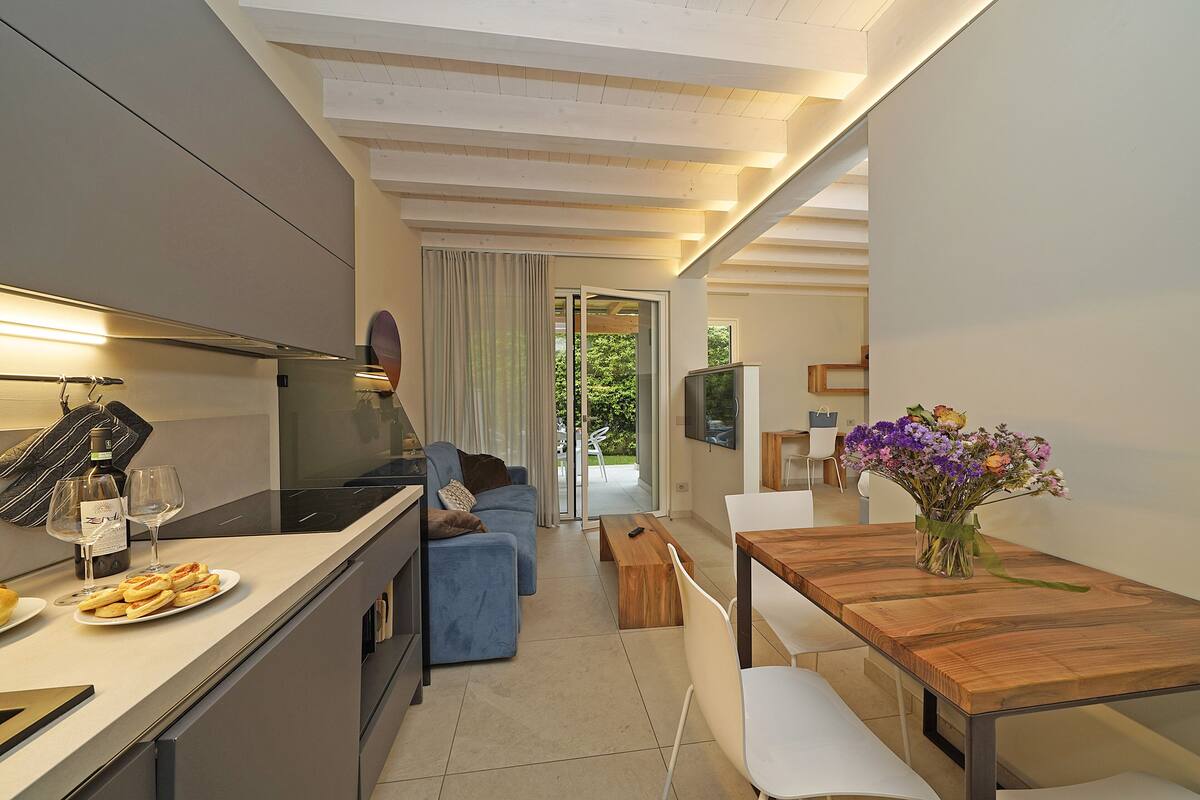 A modern kitchen with a dining area, a sofa, and a wooden table with a vase of flowers.