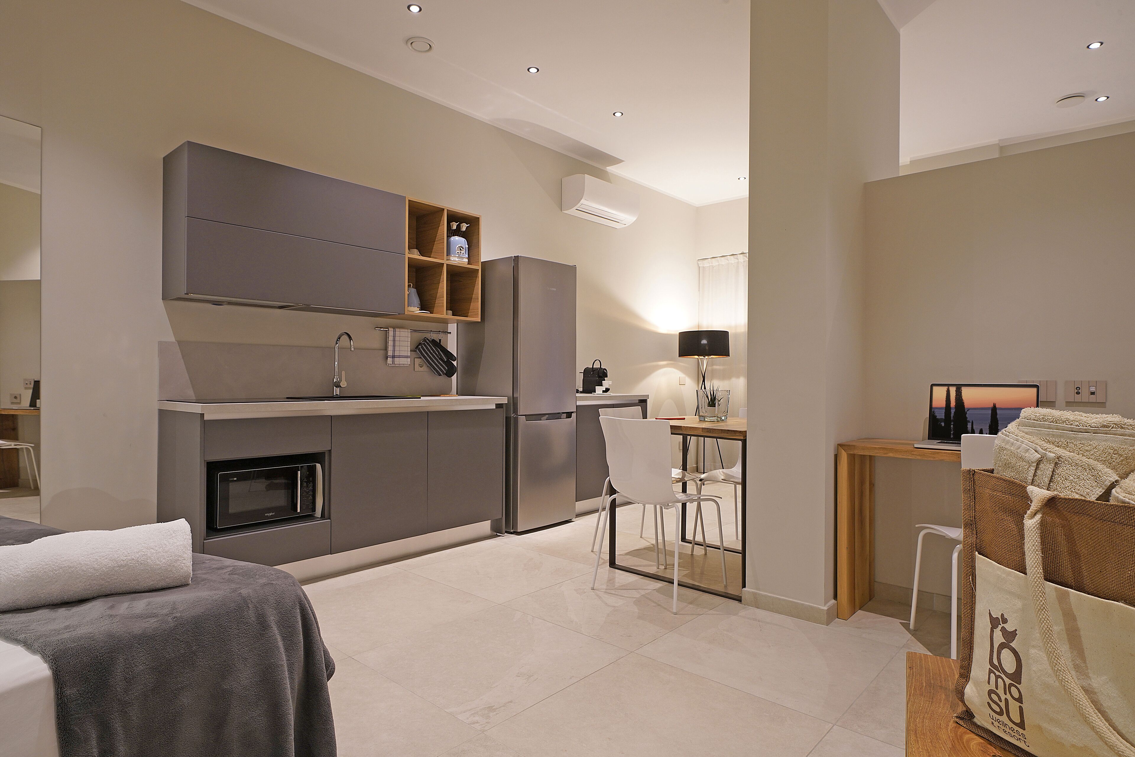 A modern kitchen with grey cabinetry, a built-in oven, and a refrigerator. There is a dining area with a table and chairs, and a laptop on the table.
