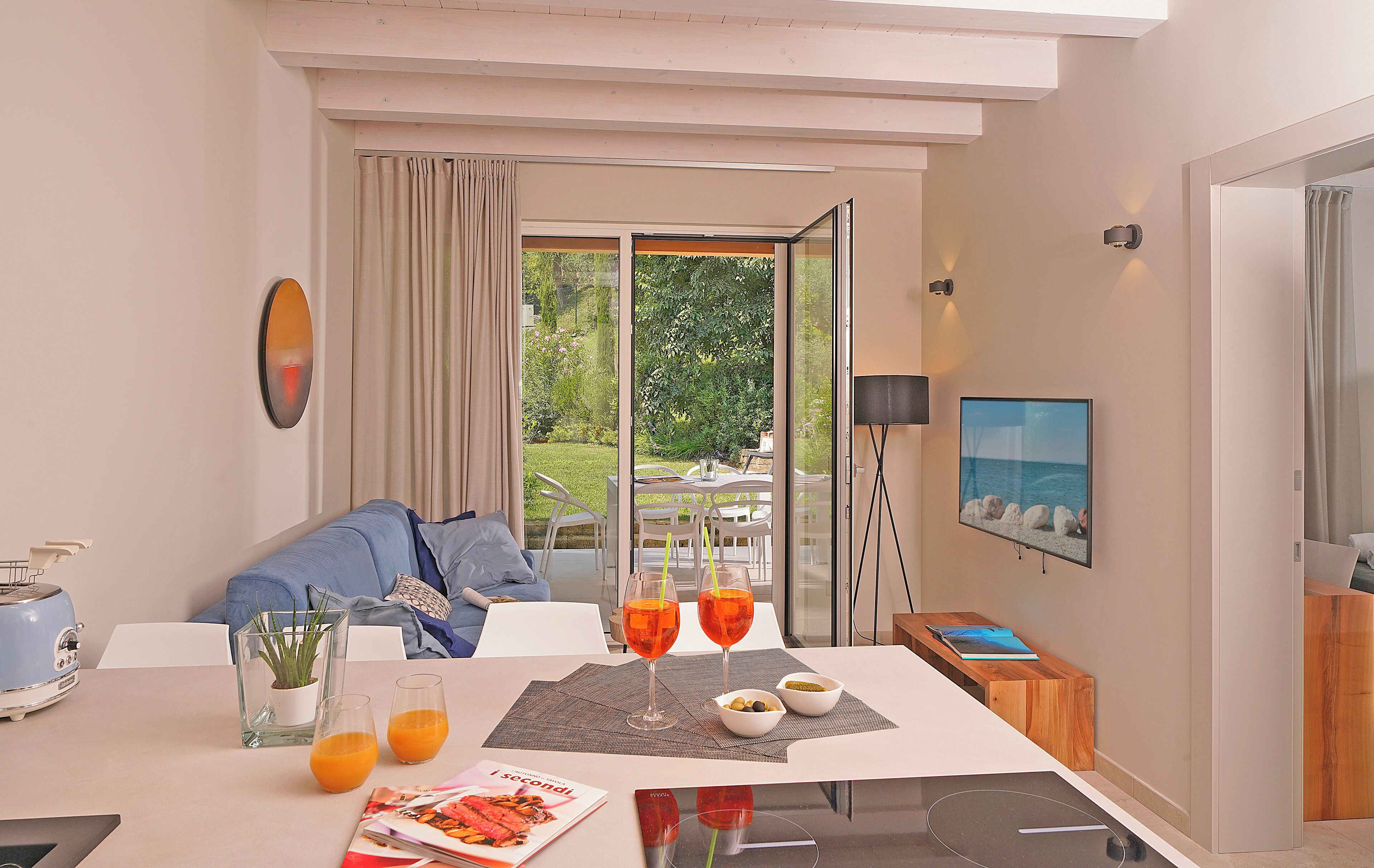 A modern hotel room with a dining area, a sofa, a TV, and a view of the outdoors.