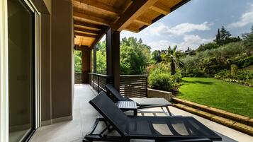 A covered patio with two lounge chairs, a wooden ceiling, and a view of a well-maintained garden.
