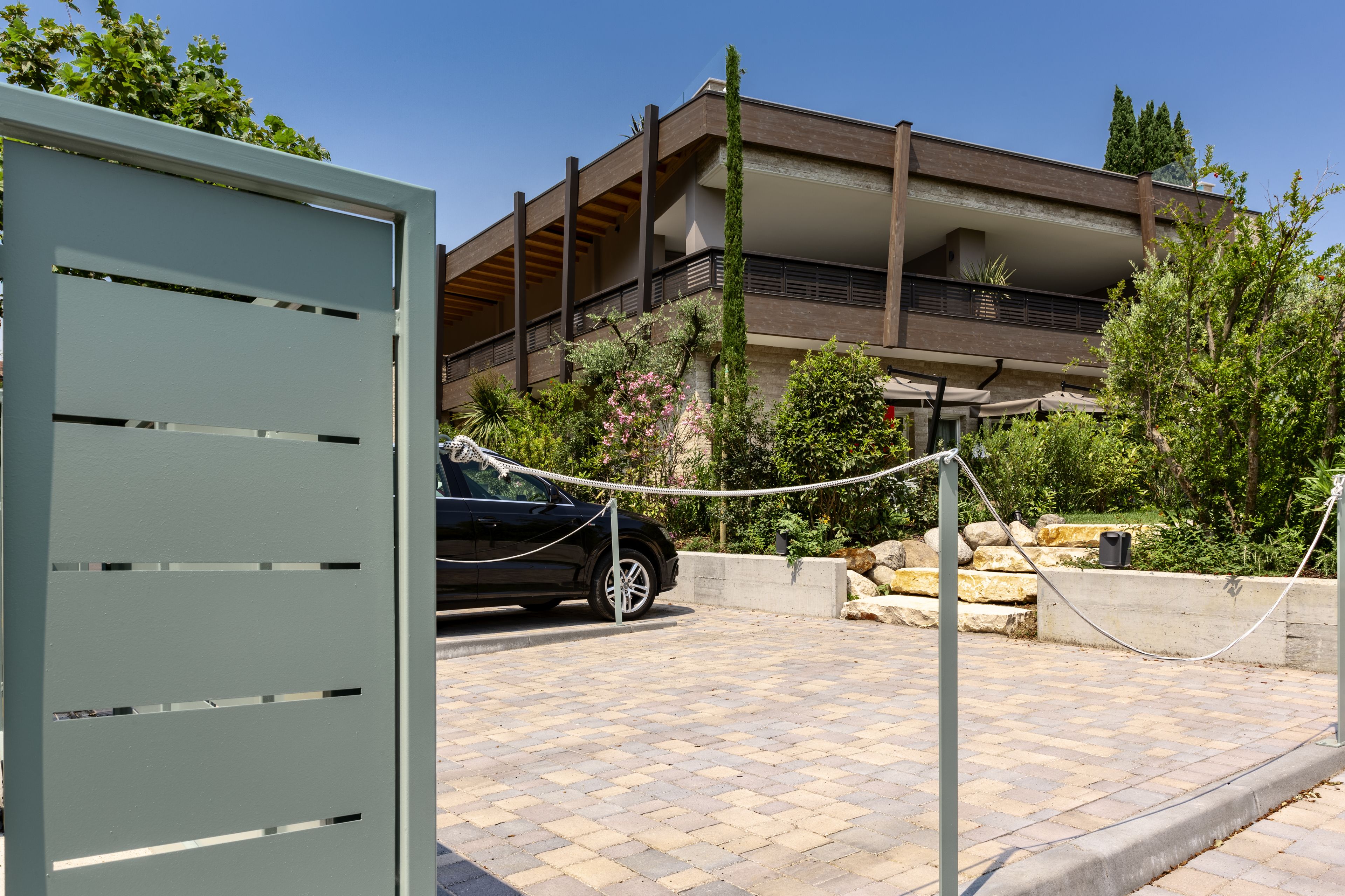 A modern building with a balcony, a car parked in front, and a stone wall with greenery.