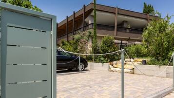 A modern building with a balcony, a car parked in front, and a stone wall with greenery.