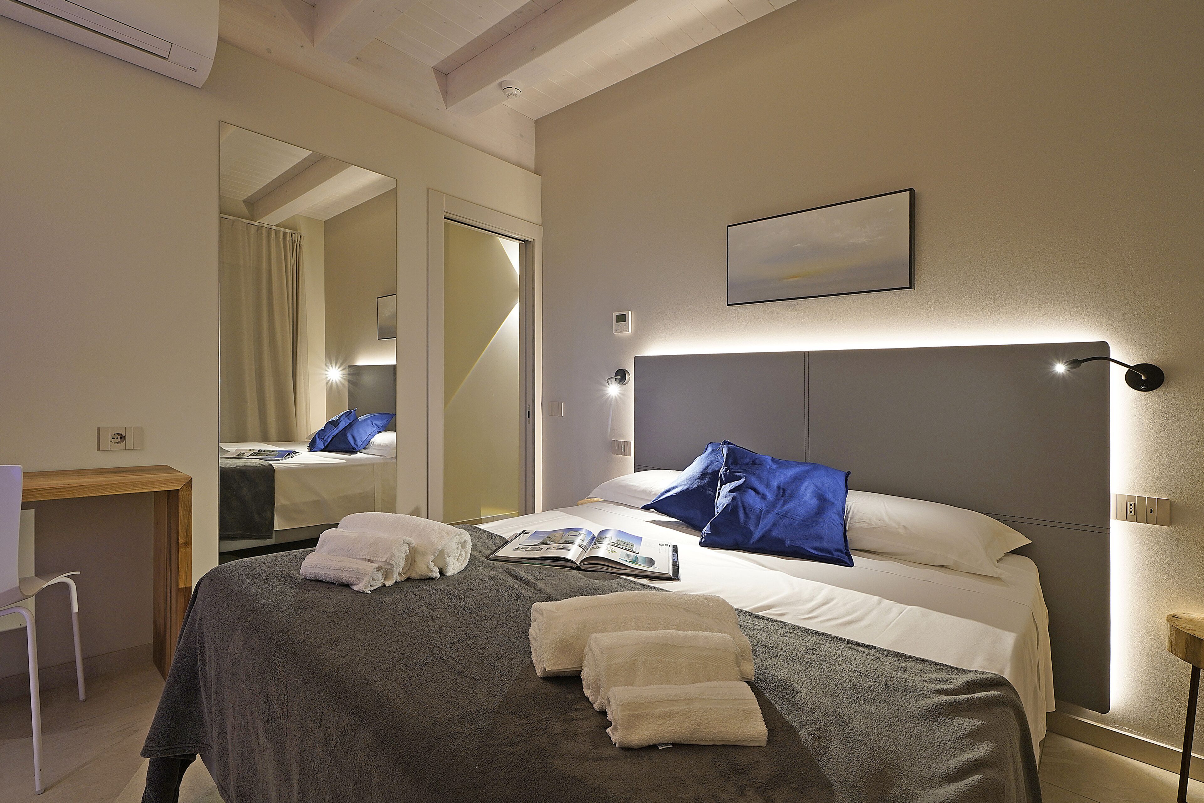 A neatly made bed with towels, a bedside table, a reading lamp, and a large mirror.