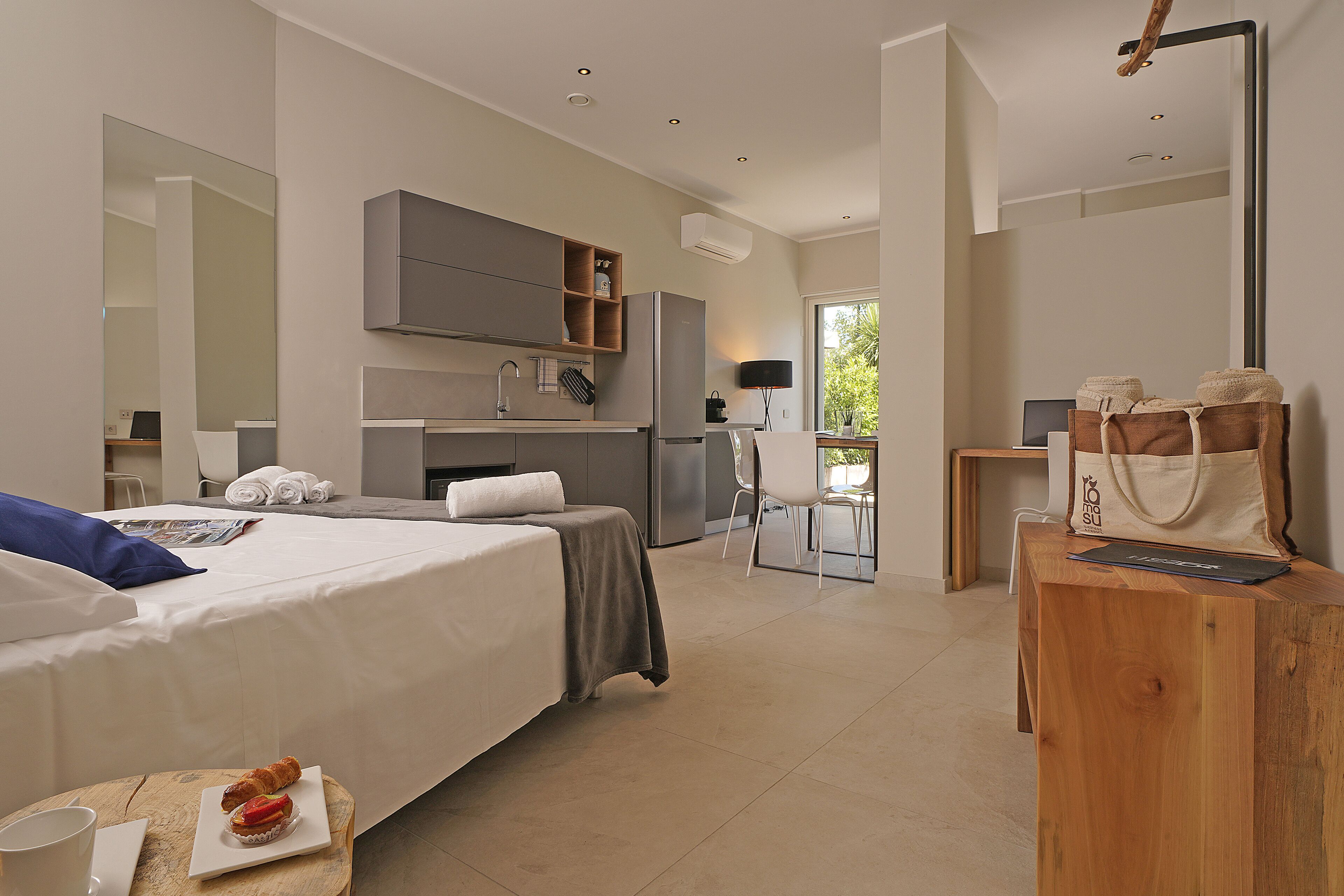 Una habitación de hotel moderna con una cama grande, un escritorio de madera, una kitchenette y vistas al exterior.