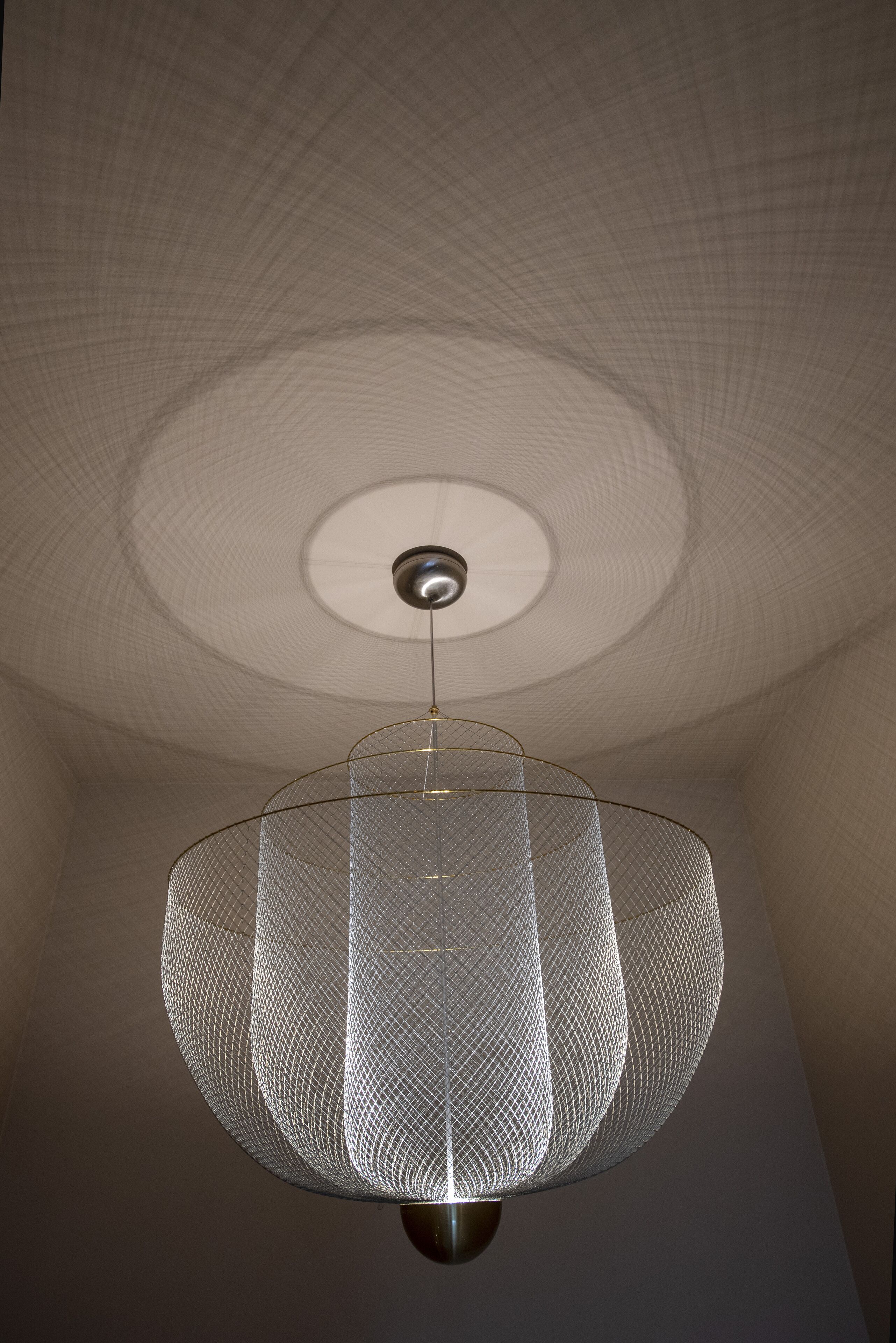 A modern ceiling with a circular design and a hanging light fixture with a wireframe structure.