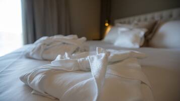 A neatly made bed with white linens and pillows, a headboard, and a window with curtains.