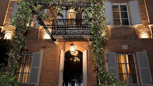 A building facade with a black door, white shutters, and a wrought iron balcony with climbing plants.