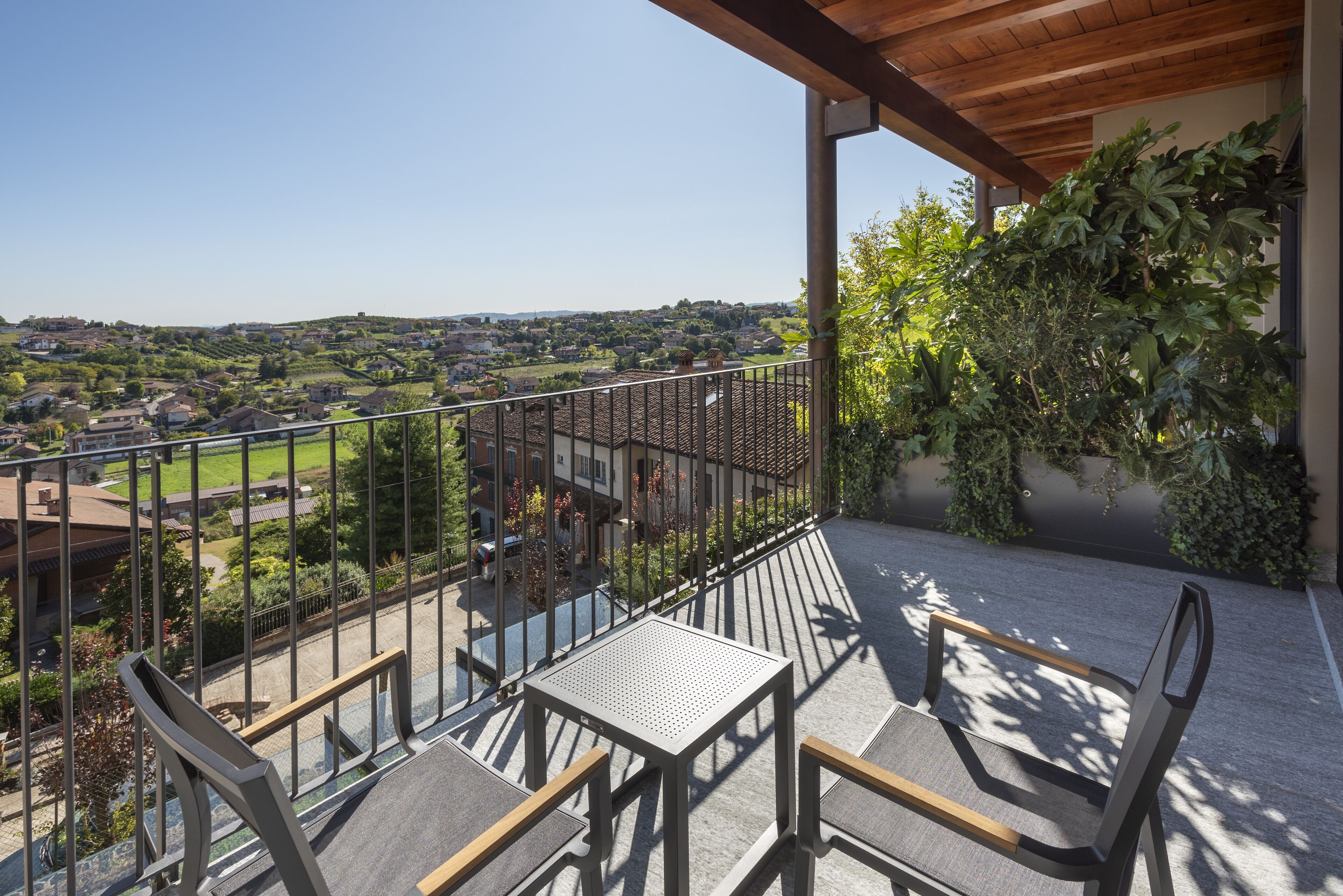 A balcony with a table and chairs, overlooking a residential area with houses and greenery.