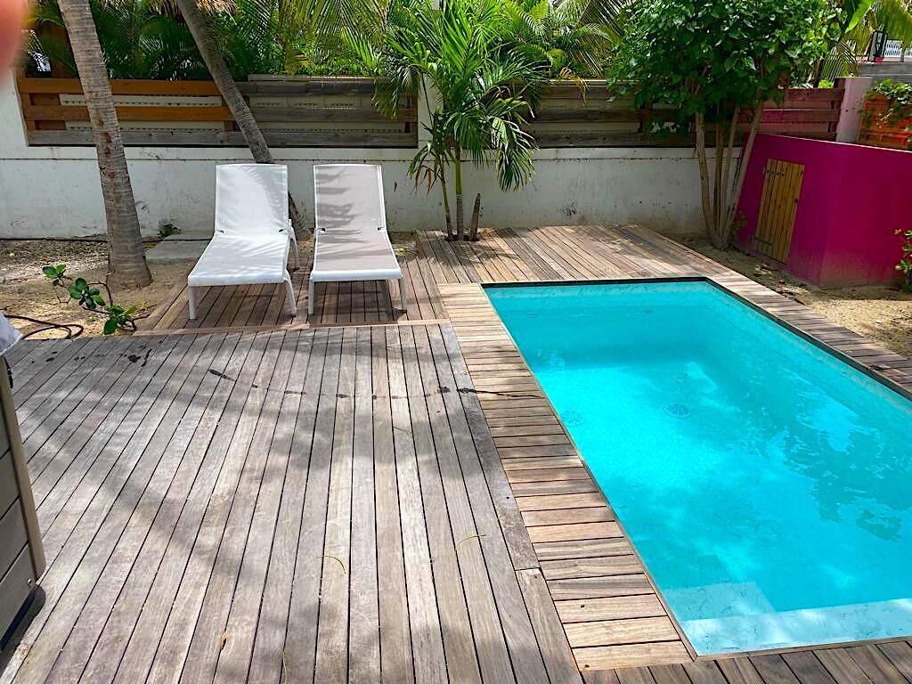 Una terraza de madera con dos sillones blancos y una piscina.