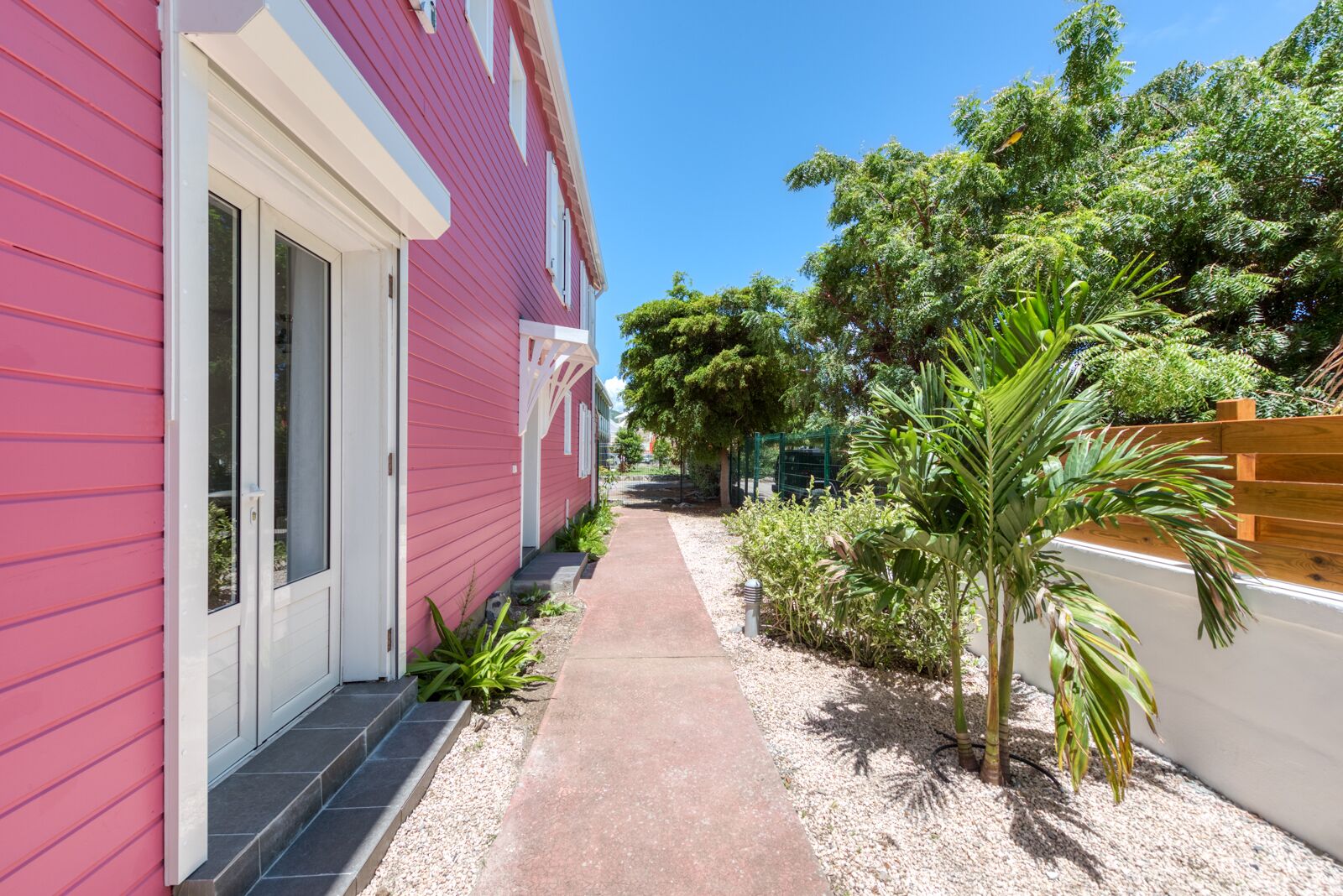 A narrow pathway flanked by a pink building and a white wall with a wooden fence.
