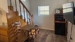A dining area with a wooden staircase, a small window, and a kitchenette with a microwave and refrigerator. - Room 1- Historic Little Switzerland (Jasper)