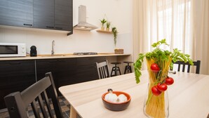 A modern kitchen with dark cabinets, a microwave, and a dining table with chairs. There is a vase with tomatoes and a bowl of garlic on the table.