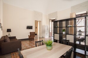 A living room with a sofa, a dining table with chairs, a TV, and a bookshelf.