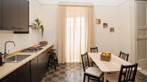 A compact kitchen with a dining area, featuring a checkered floor, a wooden table, and a window with curtains.