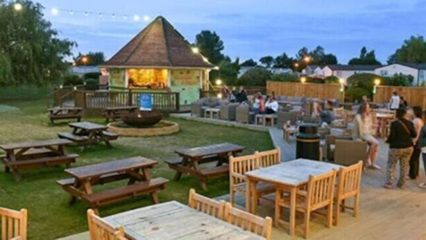 An outdoor patio area with wooden tables and chairs, a barbecue grill, and a small gazebo. - Gold Standard Caravan - SOUTH VIEW PARK (Skegness)