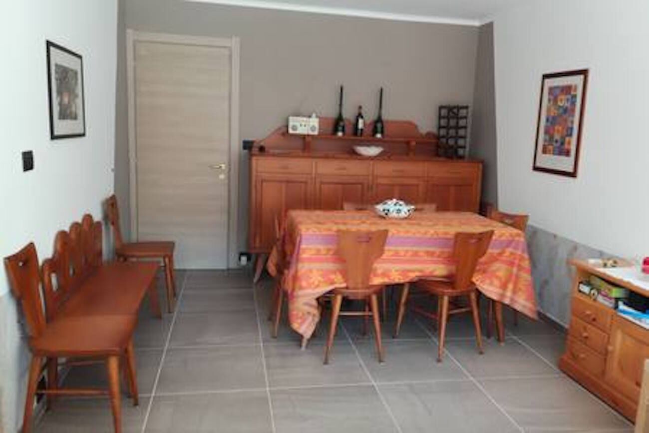 Un'area pranzo con un tavolo apparecchiato per quattro persone, sedie in legno, un armadietto con stoviglie e una porta sullo sfondo.