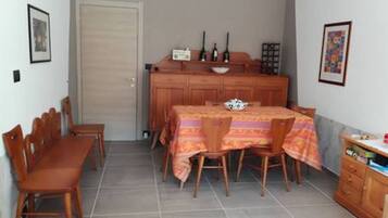 Un'area pranzo con un tavolo apparecchiato per quattro persone, sedie in legno, un armadietto con stoviglie e una porta sullo sfondo.