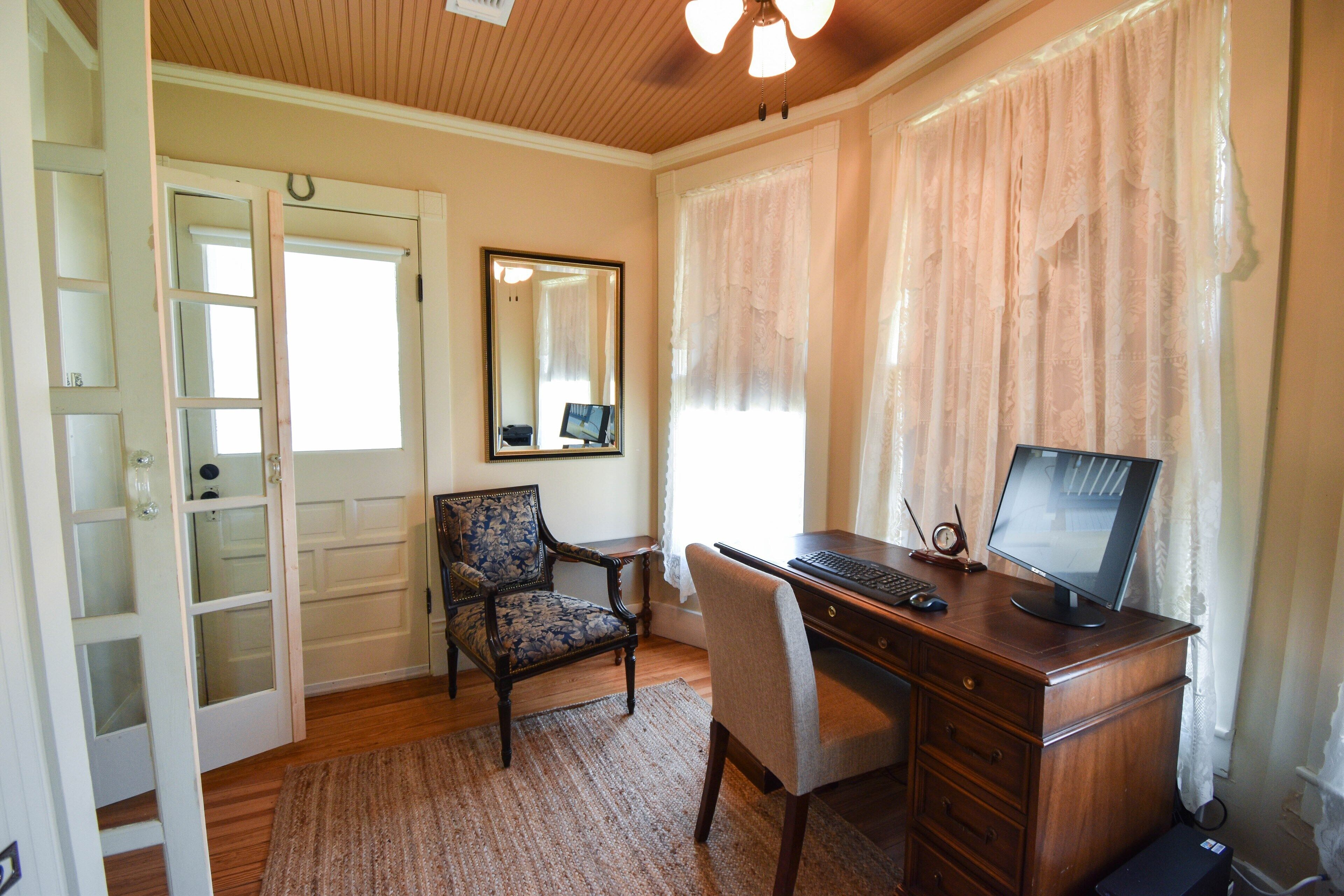 A room with a wooden desk, a computer, a chair, a mirror, and a door with glass panels.