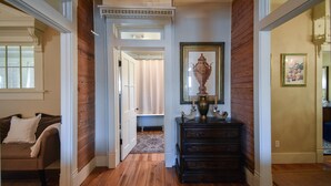A hallway with wooden flooring, a dark wooden dresser, a mirror, and a framed picture on the wall.