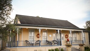 A two-story house with a porch, a covered front porch area with chairs, and a small garden with potted plants.