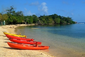 A beach with kayaks lined up on the sand, a clear blue sky, and a forested island in the background. - Calabash Bight Resort (Roatan)
