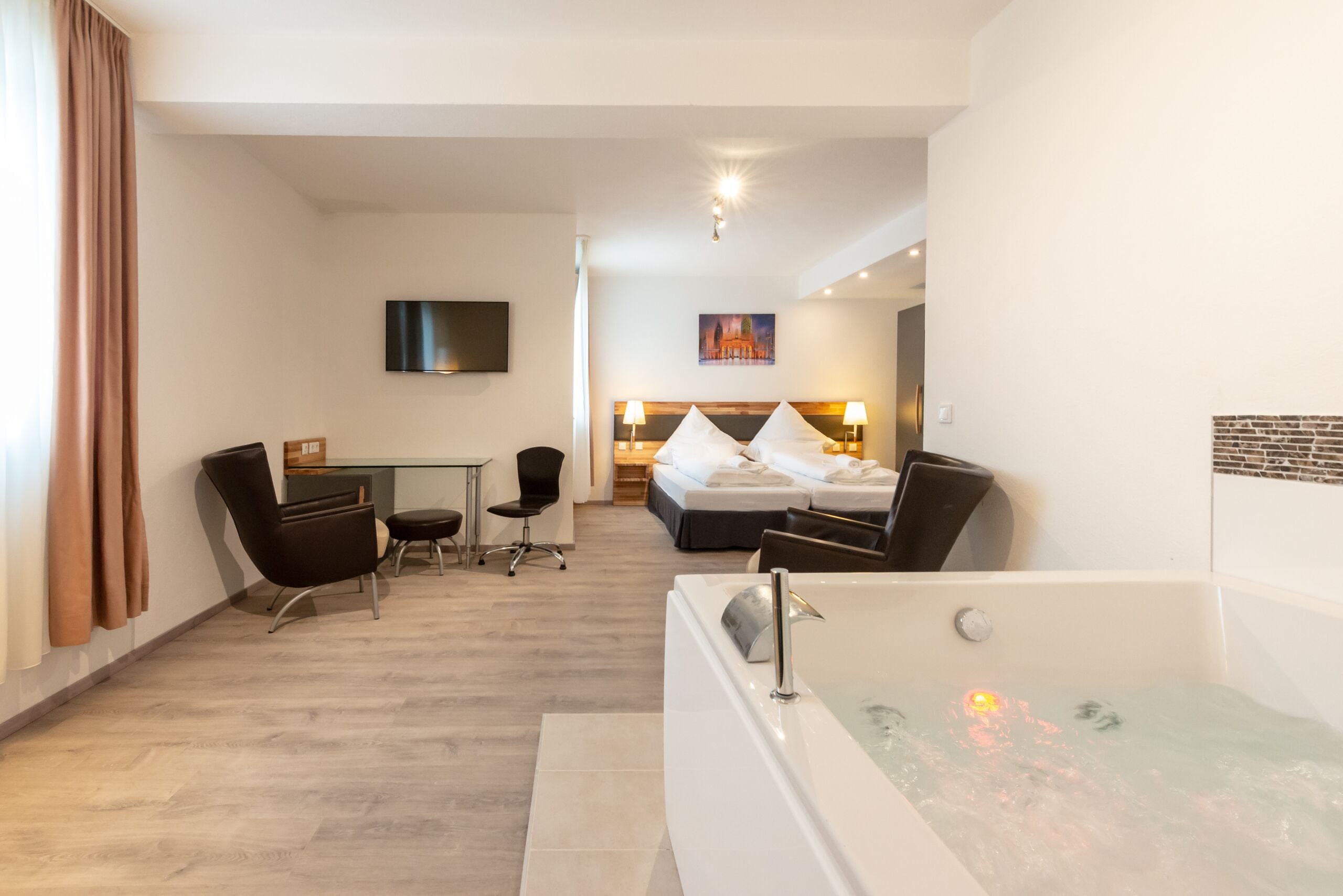 Ein Hotelzimmer mit einer großen Badewanne, einem Schreibtisch mit Stuhl, einem Bett mit Kissen und einem flachbildfernseher an der Wand.