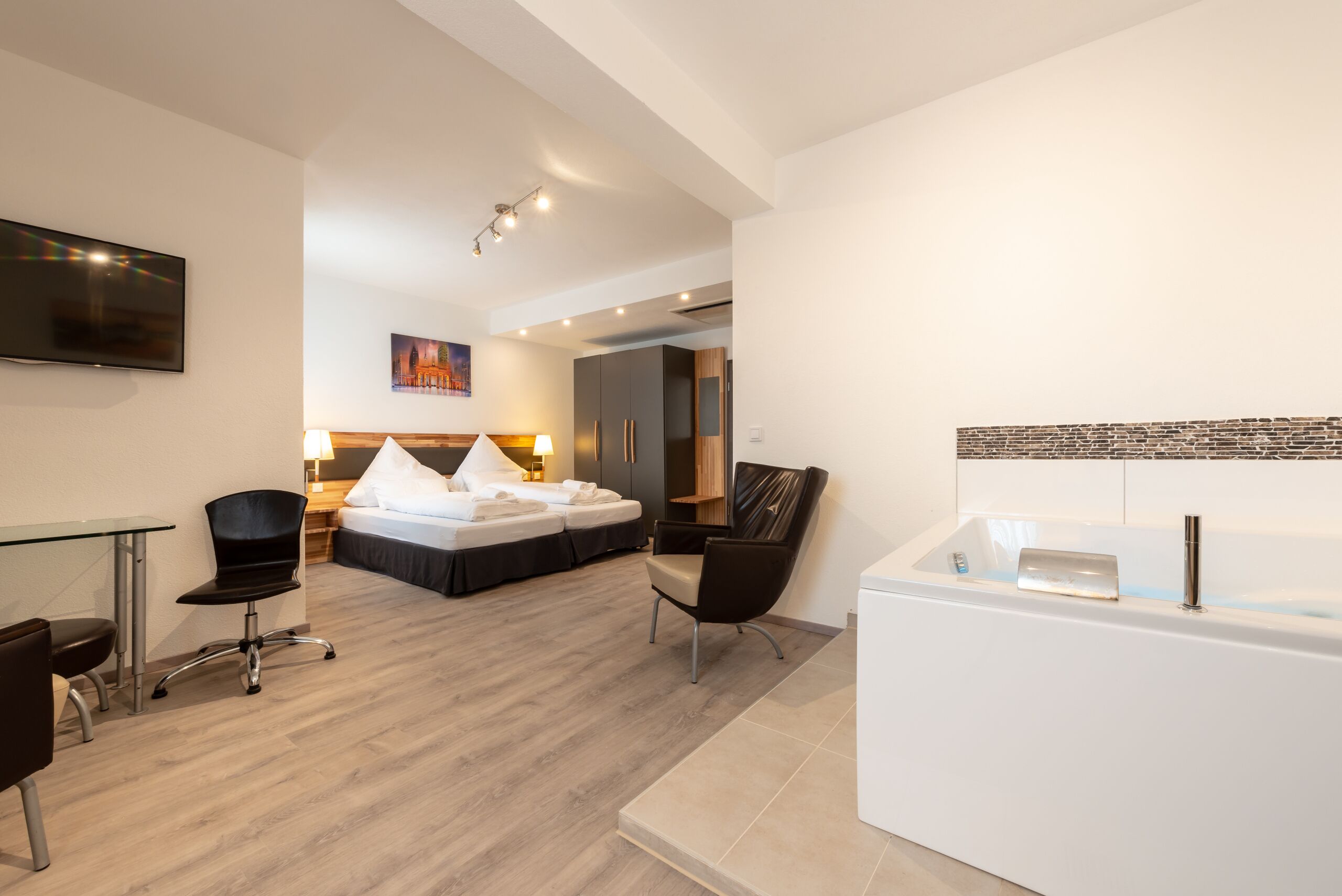 A modern hotel room with a bed, a desk, a chair, a bathtub, and a TV.