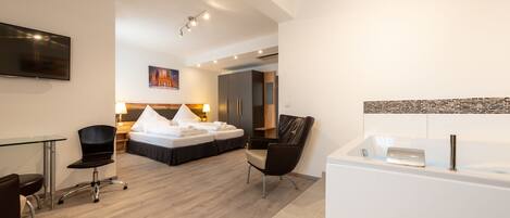 A modern hotel room with a bed, a desk, a chair, a bathtub, and a TV.