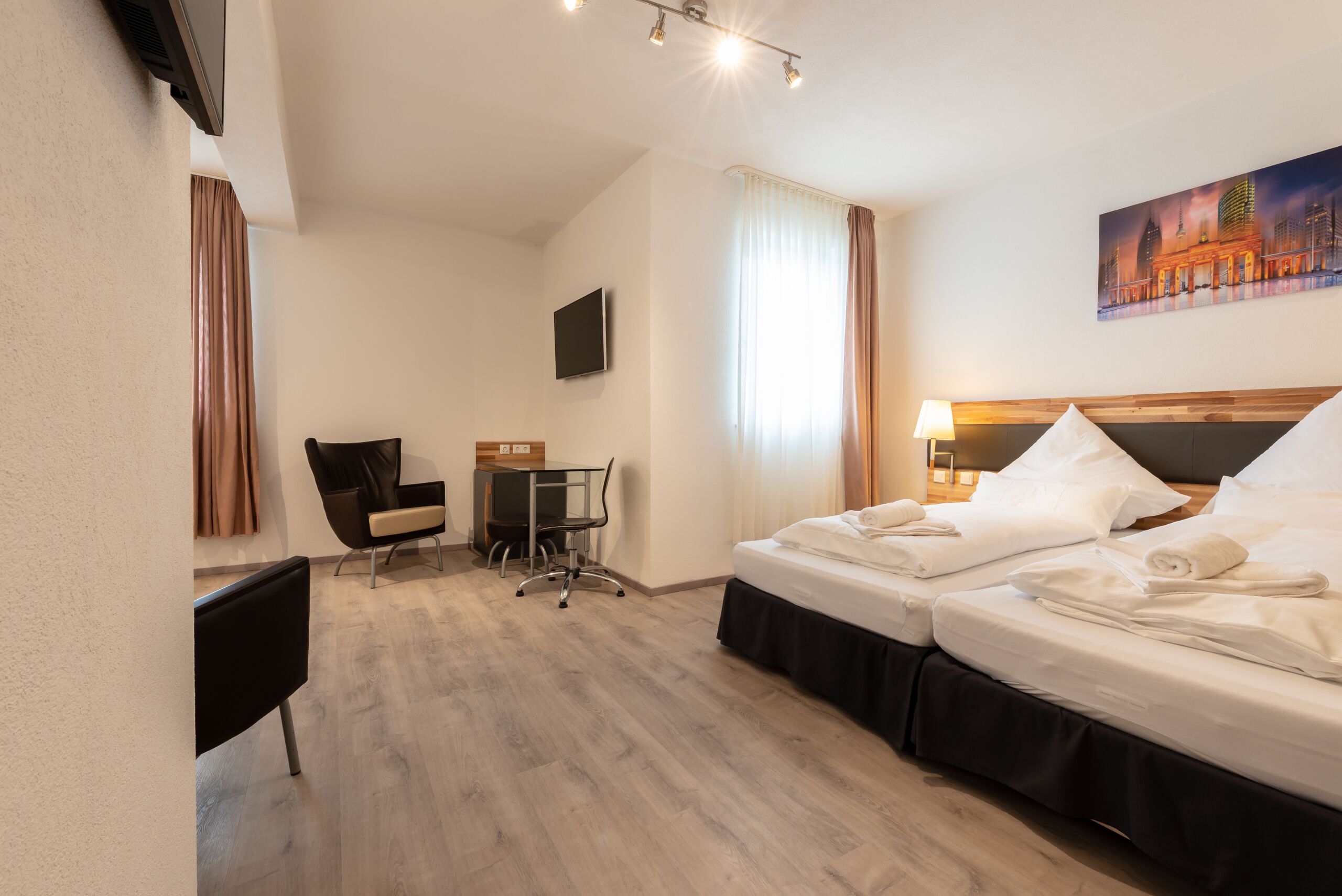 A hotel room with two beds, a desk, a chair, a TV, and a painting on the wall.
