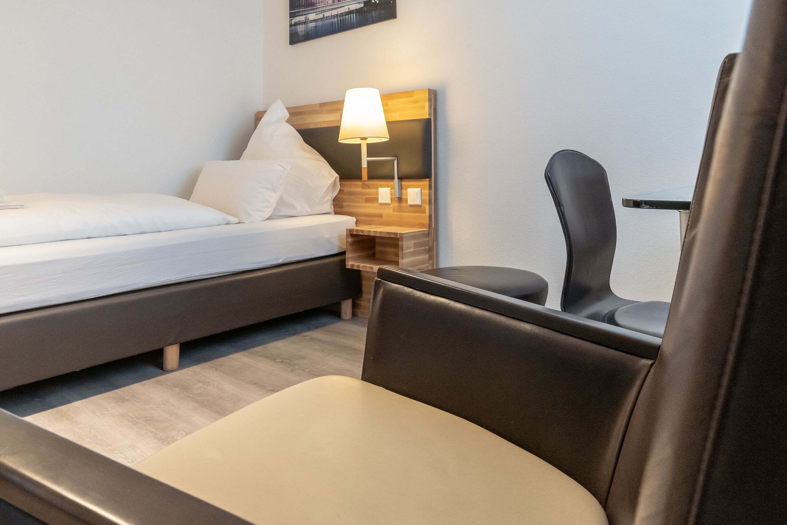 A hotel room with a bed, a chair, a nightstand with a lamp, and a small table.