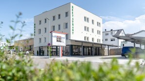 Un hotel moderno con restaurante en la planta baja, que cuenta con una entrada accesible y un área de estar al aire libre techada.